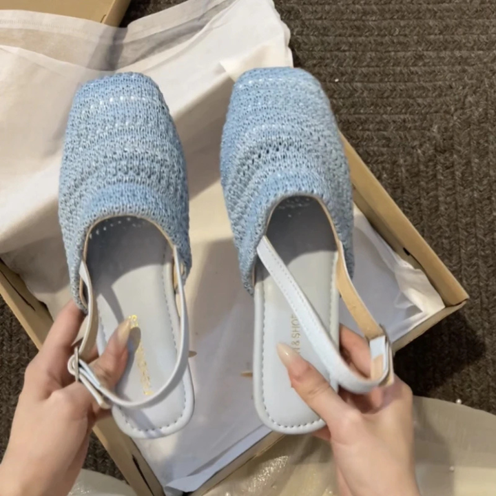 Pair of blue textured slippers being held above an open cardboard box.