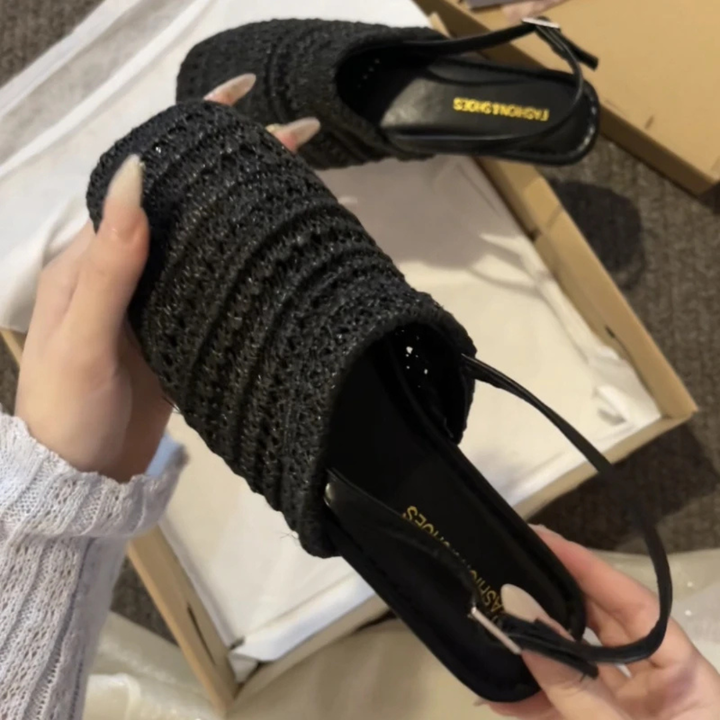 Black knitted slides being held with a box in the background