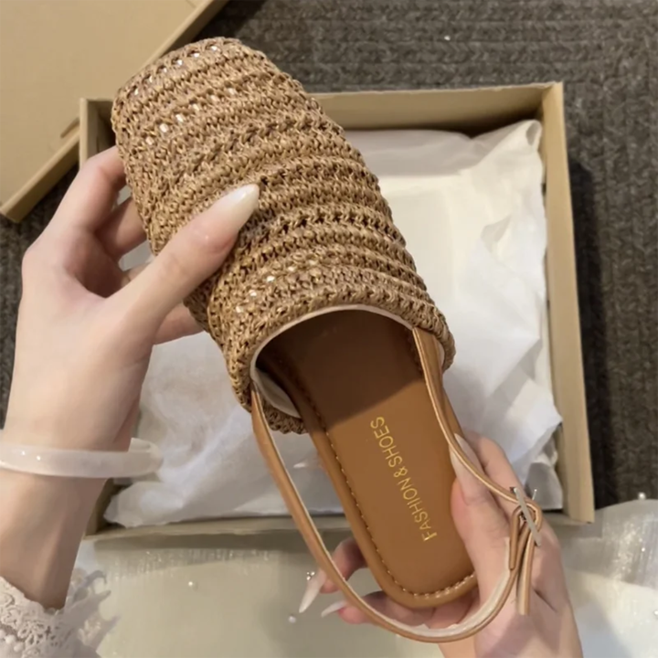Hand holding a Brown woven sandal against a neutral background.