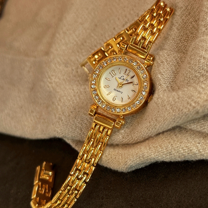 Gold wristwatch with diamond accents on a beige fabric background