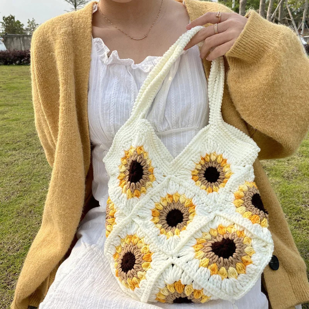 Person holding a beige crochet bag with sunflower pattern outdoors