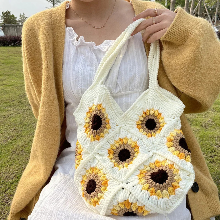 Person holding a beige crochet bag with sunflower pattern outdoors