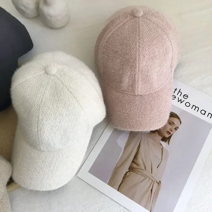 Two knit caps, one white and one pink, on a surface with a magazine underneath.