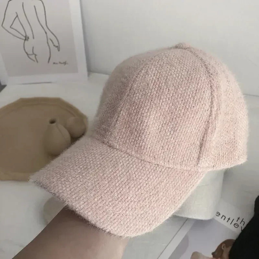Pink knitted cap held by a hand on a light background