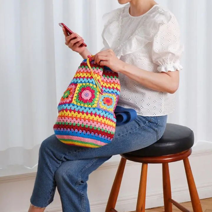 Person sitting on a stool holding a blue crocheted bag.