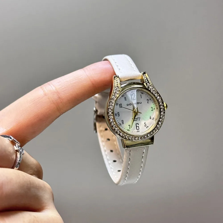 White wristwatch with gold accents held by a finger against a gray background