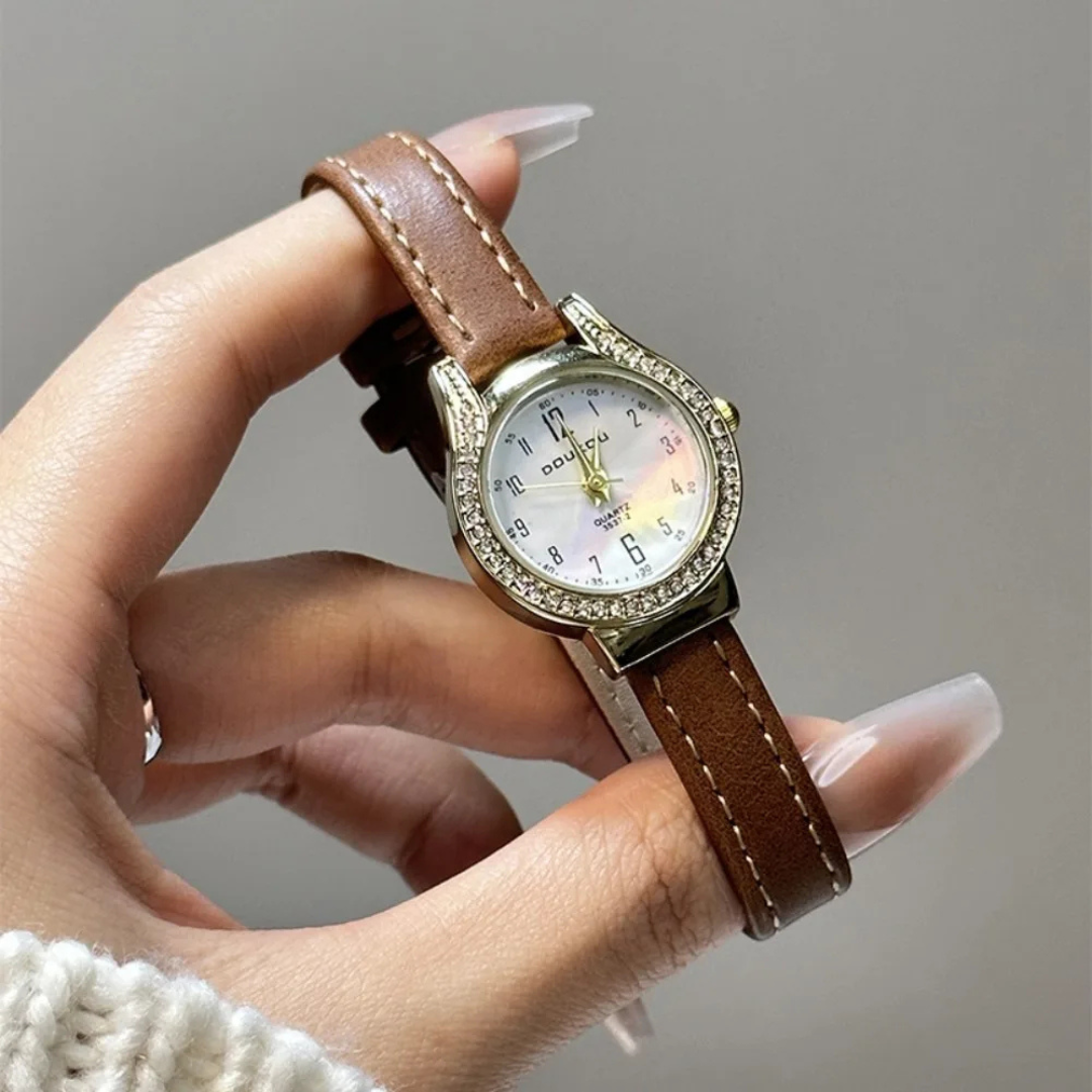 Hand holding a watch with a brown leather strap and decorative case against a neutral background
