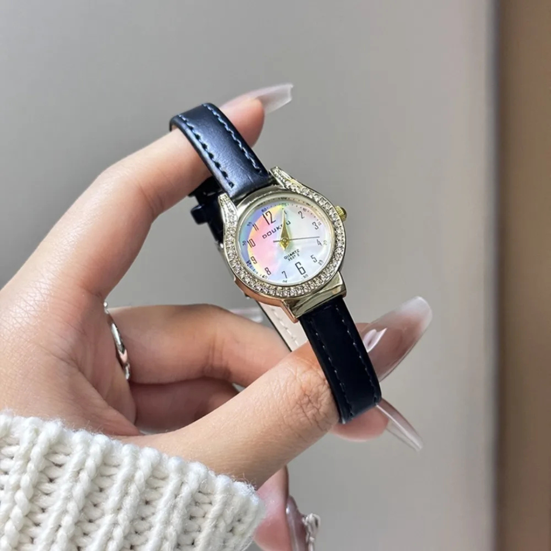 Hand holding a watch with a black strap and colorful face against a neutral background