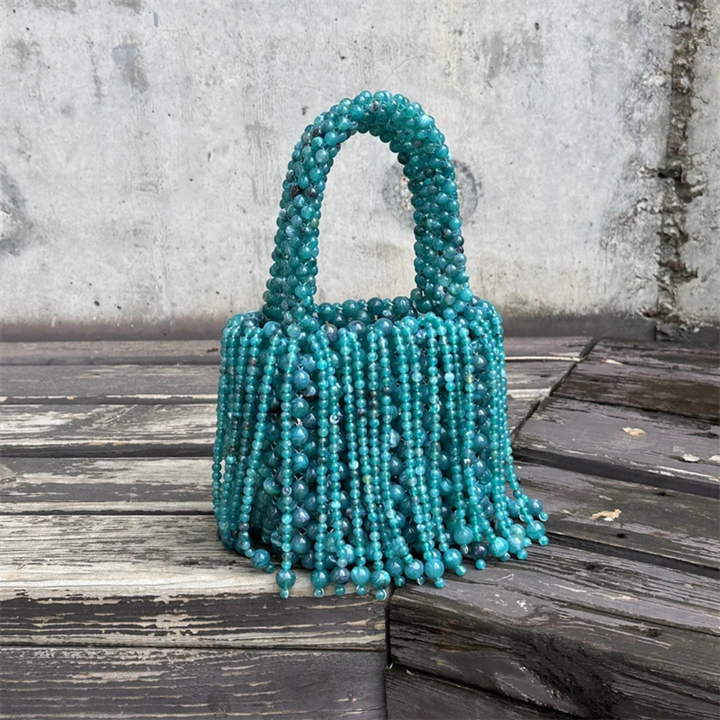 Blue beaded handbag on a wooden surface with a concrete wall background