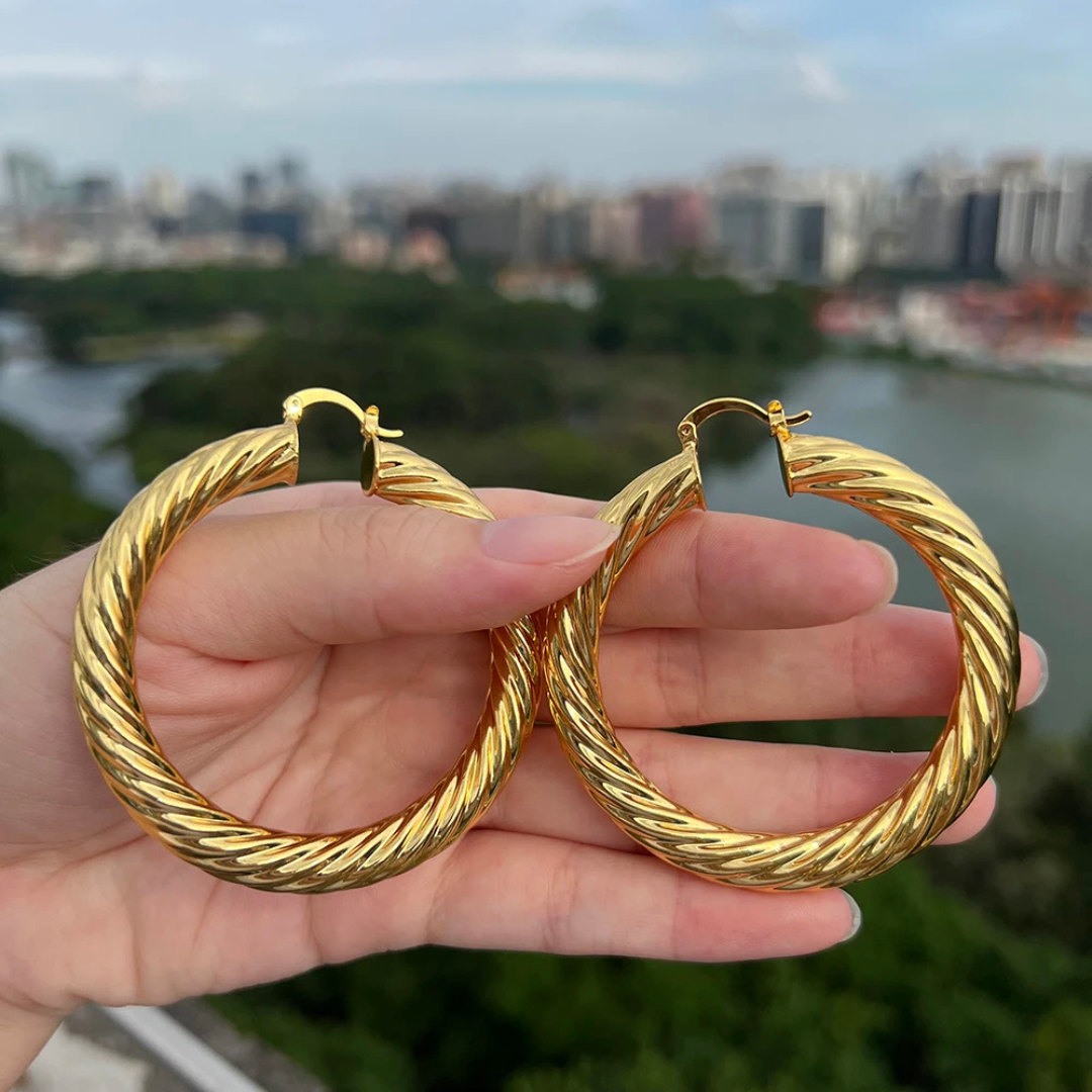 Gold hoop earrings held in a hand with a cityscape in the background