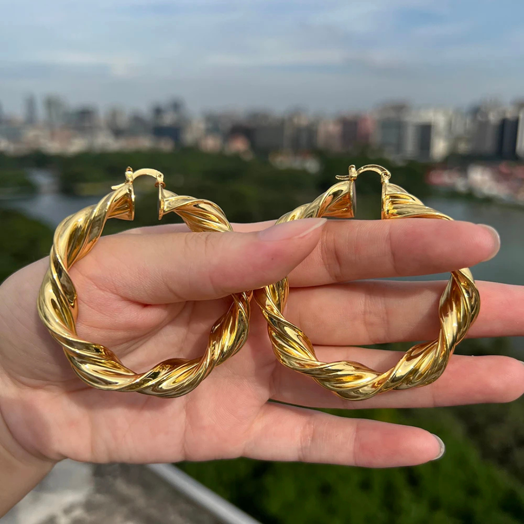 Gold hoop earrings held in a hand with a cityscape in the background