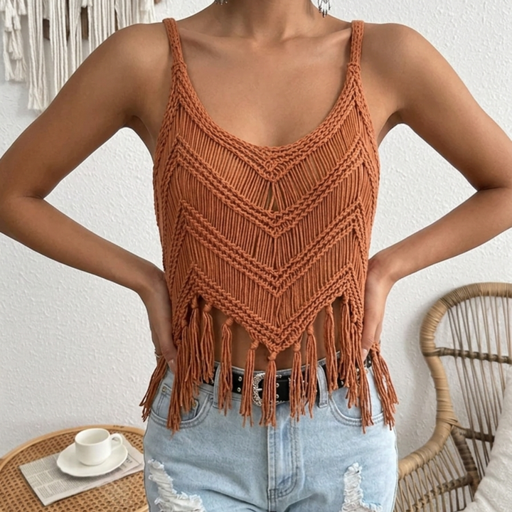 Person wearing a orange macrame top with fringes and light blue jeans indoors.