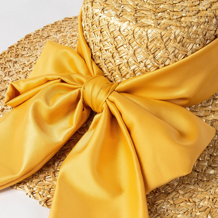 Straw hat with a large yellow bow on a light gray background