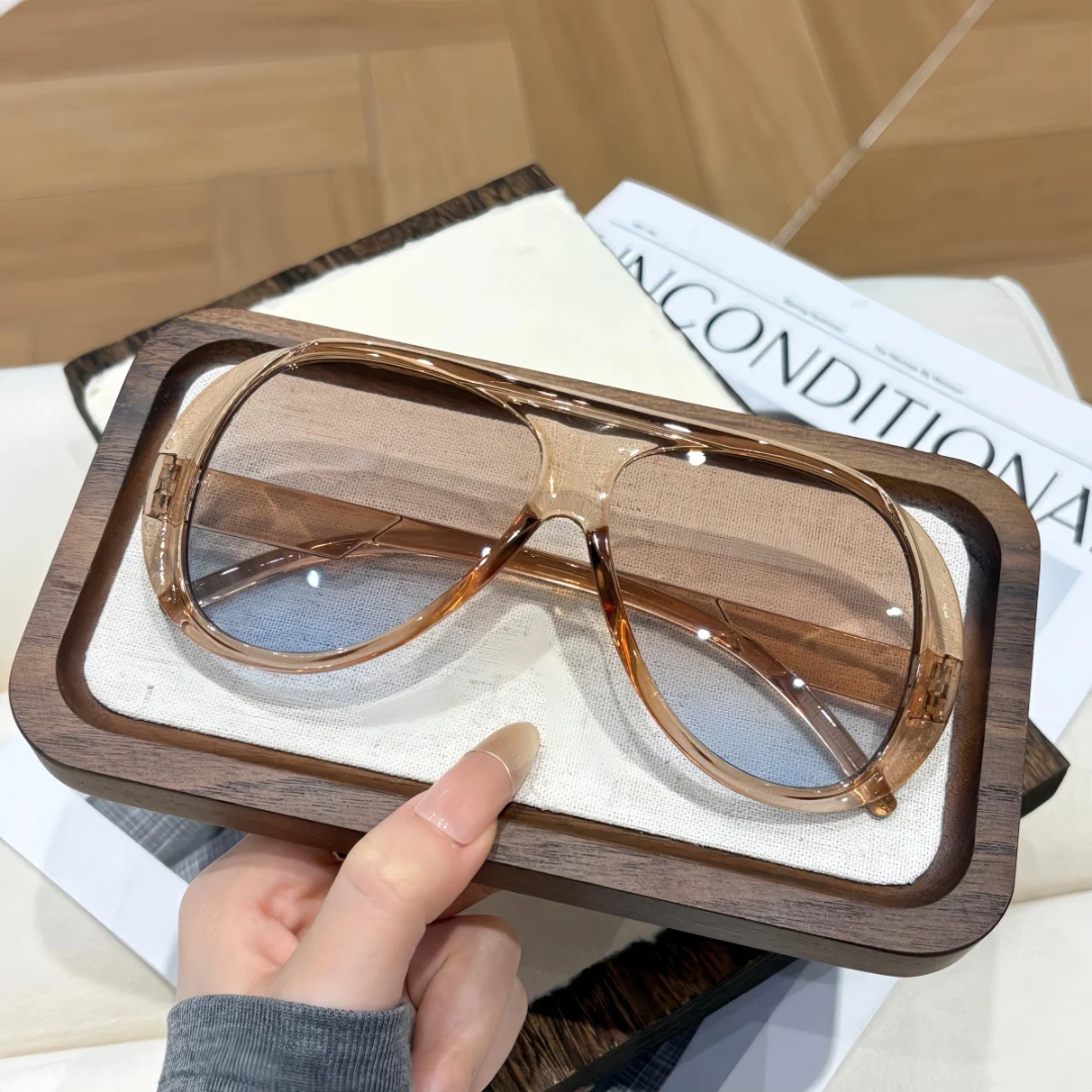 Champagne sunglasses held by a hand on top of a magazine