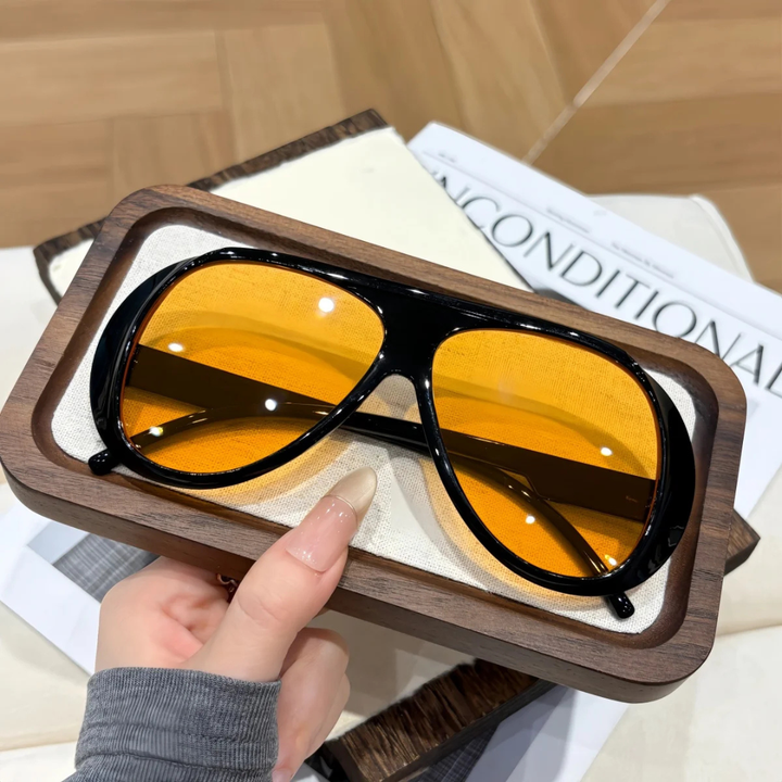 Wooden-framed sunglasses with black yellow lenses held by a hand on a magazine background