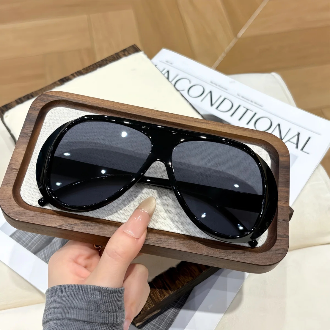 Black Gray sunglasses with a wooden frame held by a hand on top of a magazine.