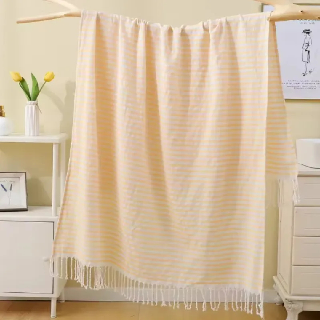 Beige striped towel with tassels draped over a chair in a room setting.
