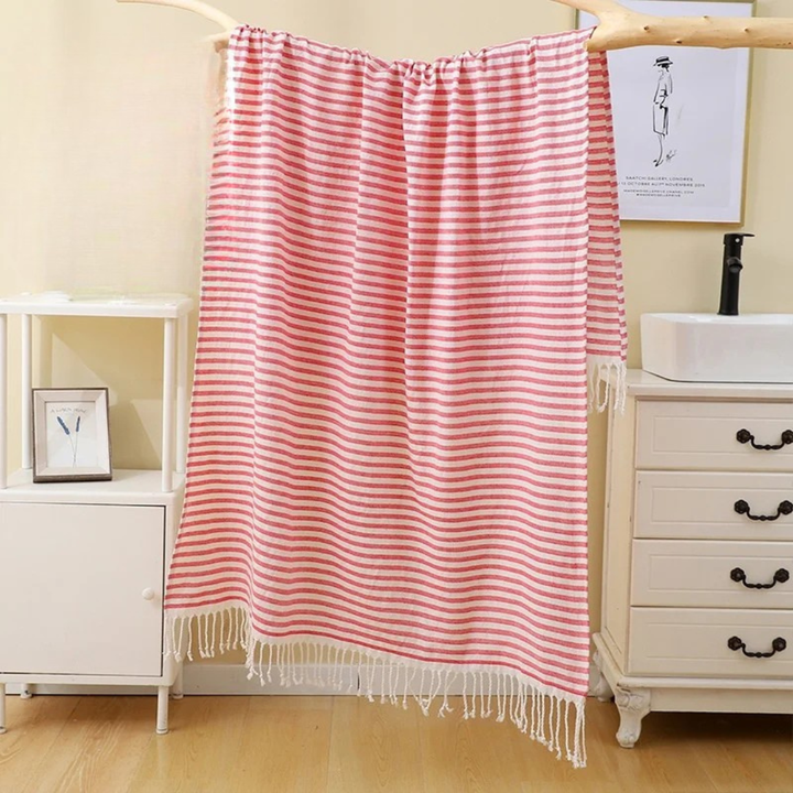 Striped pink towel hanging in a bathroom with a sink and cabinet.