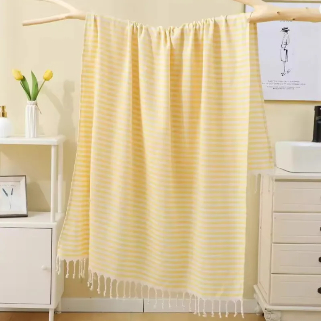 Yellow striped towel hanging on a rack with a white dresser and decor items in the background.