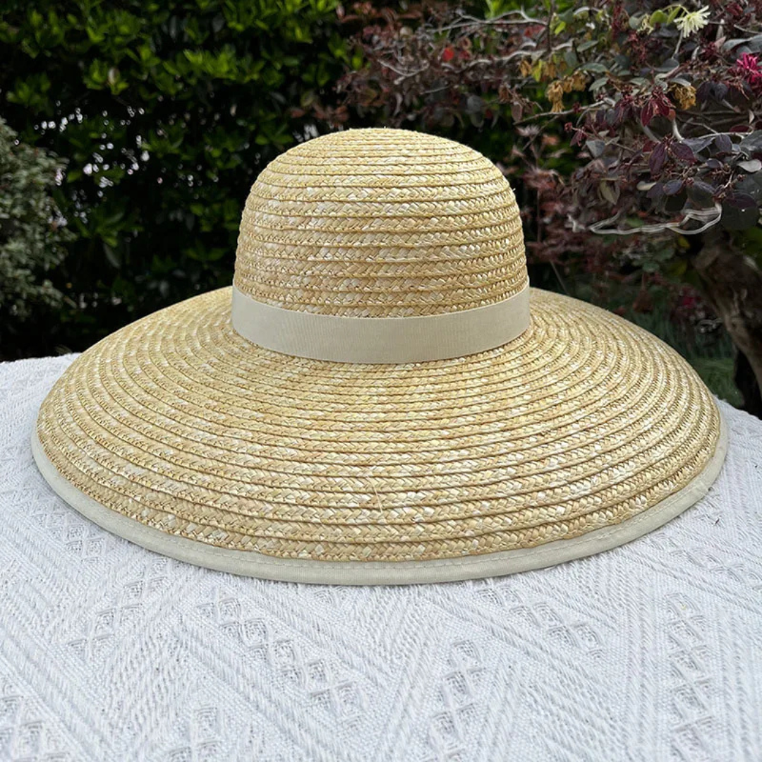 Beige straw hat with a white band on a white surface with a blurred natural background