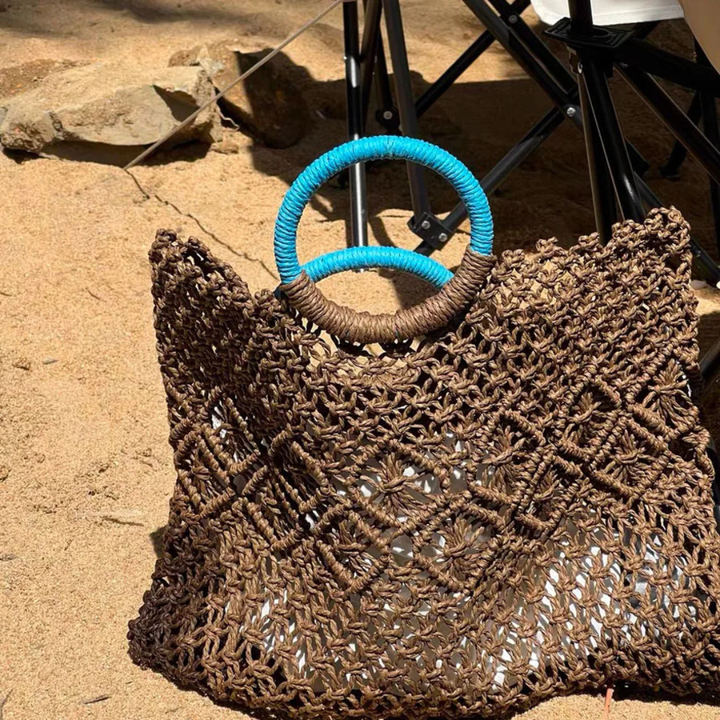 Brown woven bag with blue handle on a sandy surface