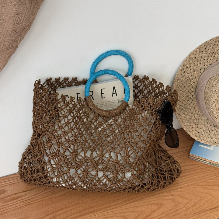 Brown woven bag with blue handle and straw hat on a wooden surface.