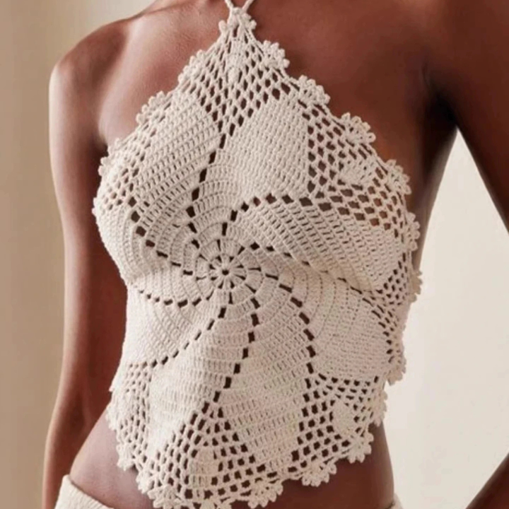 Woman wearing a crochet top and skirt with a beige clutch against a neutral background