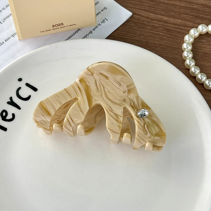 Marble-patterned hair clip on a white plate with a pearl bracelet in the background