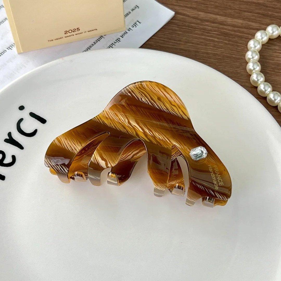 Brown hair clip on a white plate with a pearl necklace in the background