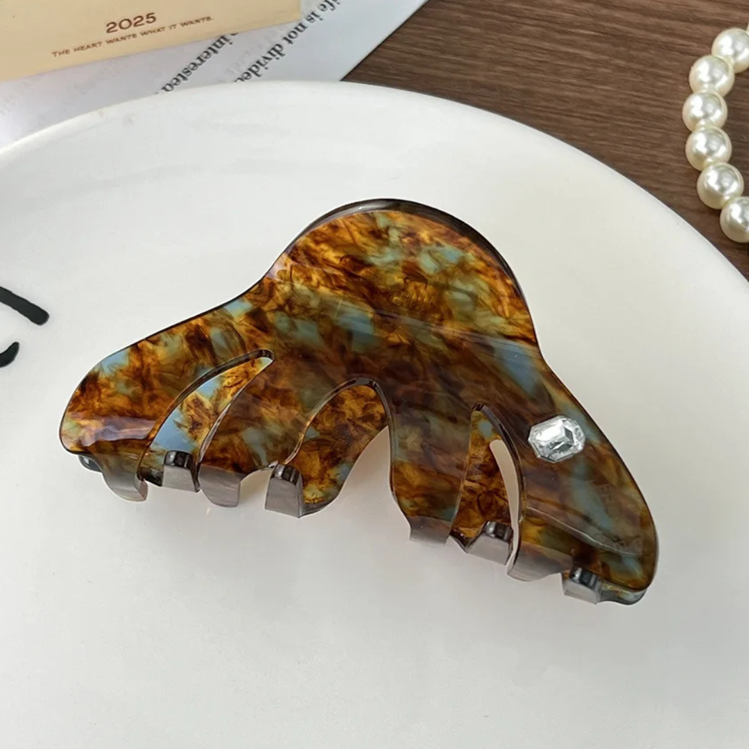 Brown tortoiseshell hair clip on a white surface with a pearl necklace in the background.