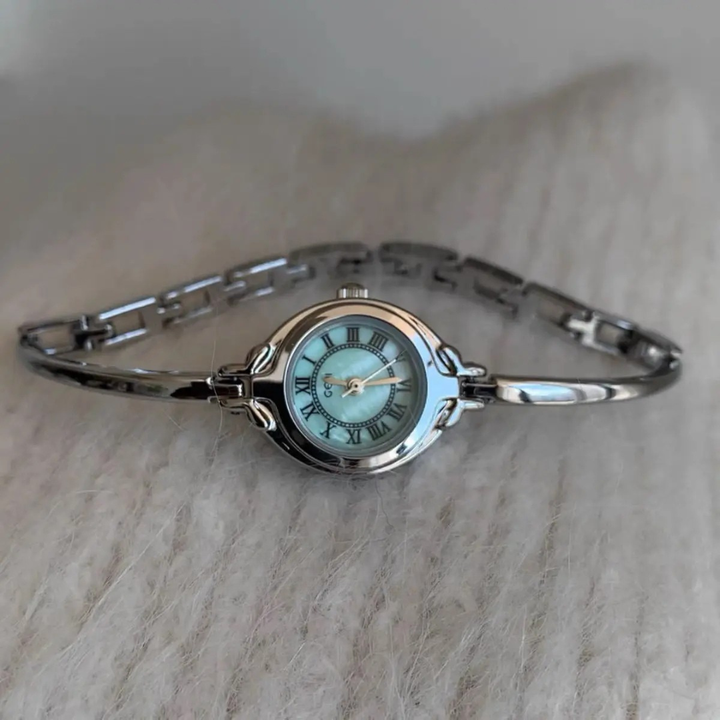 Silver bracelet watch with a light blue face on a beige surface
