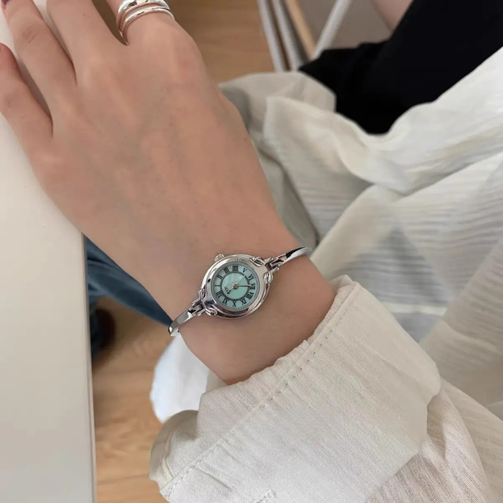 Hand wearing a silver watch with a blue face on a white sleeve.