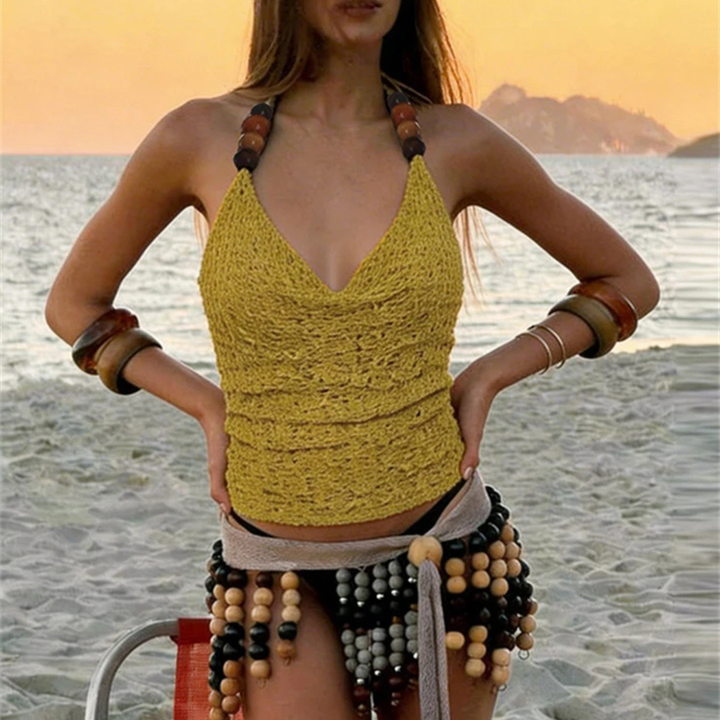 Woman wearing a yellow crochet top and beaded skirt on a beach at sunset.