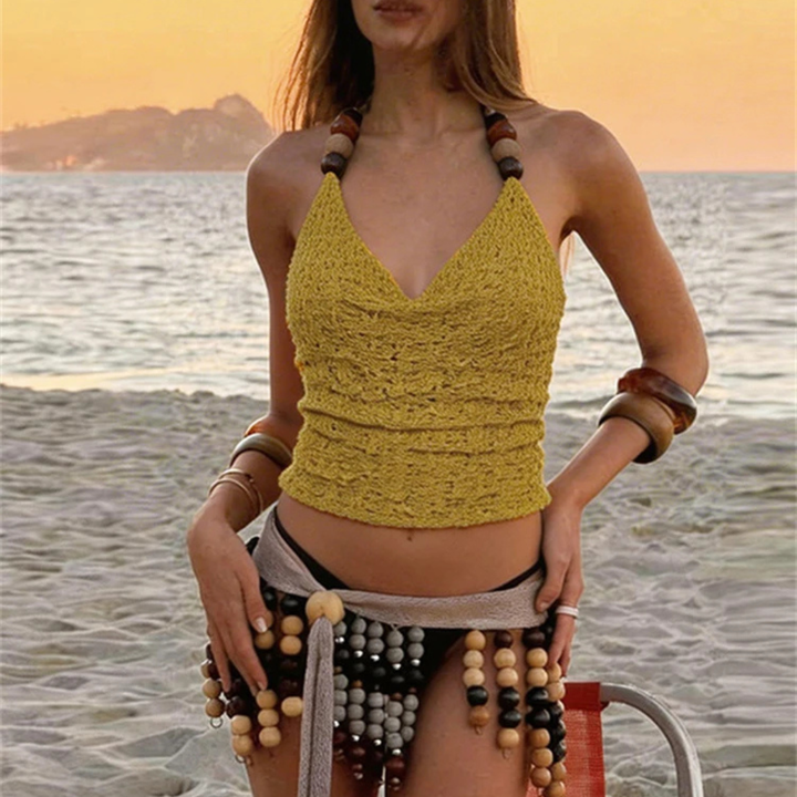 Woman in a yellow crochet top and beaded shorts standing on a beach at sunset.