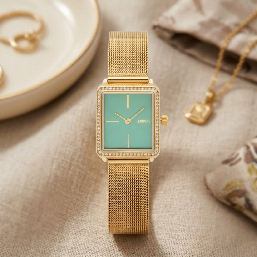 Gold watch with a green face on a textured surface with jewelry items.