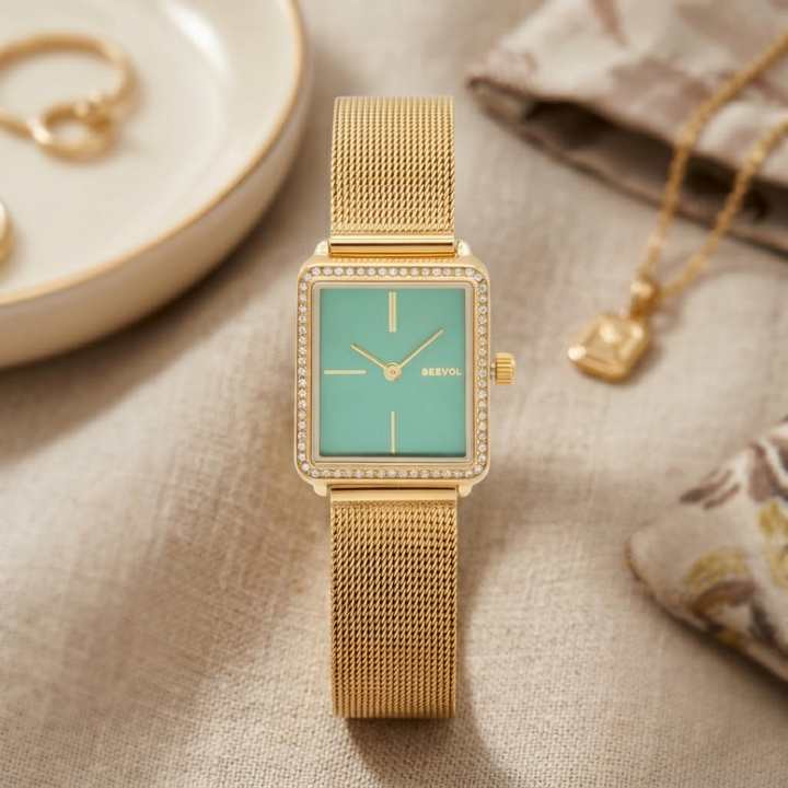 Gold watch with a green face on a textured surface with jewelry items.