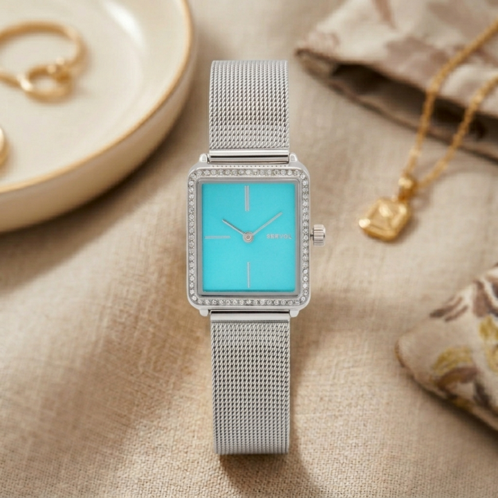Silver watch with blue face on a textured surface with jewelry items.