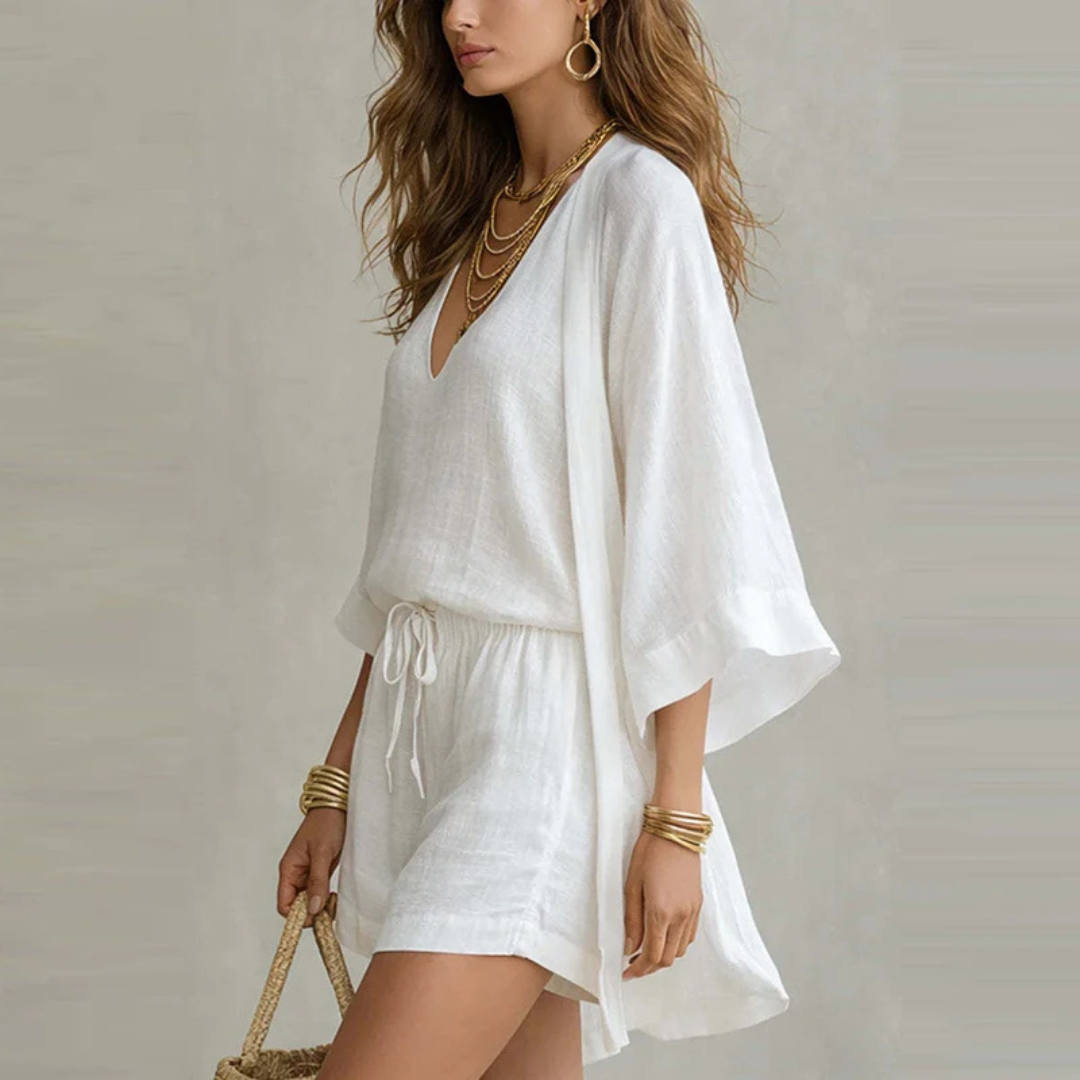 Woman wearing a white outfit with gold accessories against a neutral background