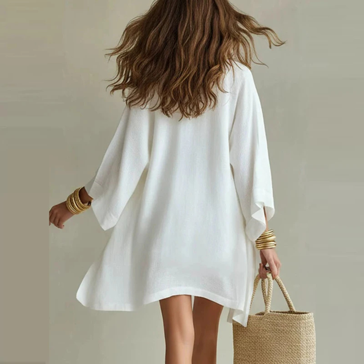 Woman wearing a white dress holding a straw bag against a neutral background