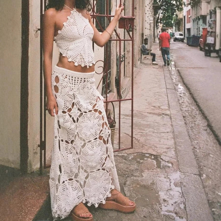 Woman wearing a crochet top and skirt with a beige clutch against a neutral background