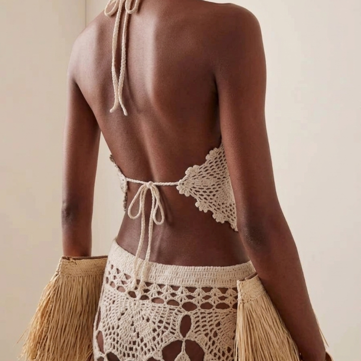 Woman wearing a crochet top and skirt with a beige clutch against a neutral background