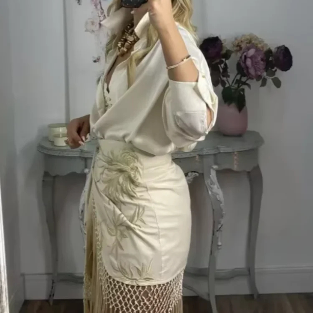 Woman in a white outfit with floral patterns standing in a room with a table and flowers.