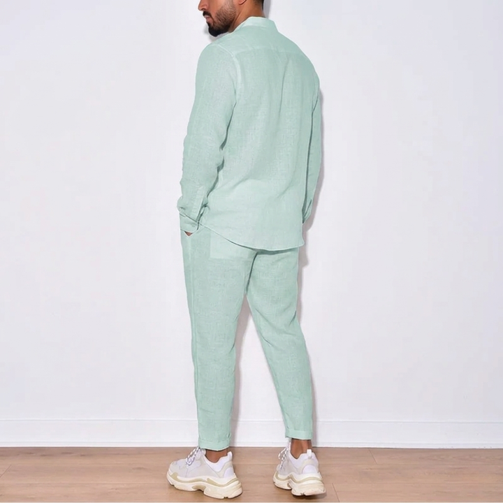 Person wearing a light green suit standing against a white wall.