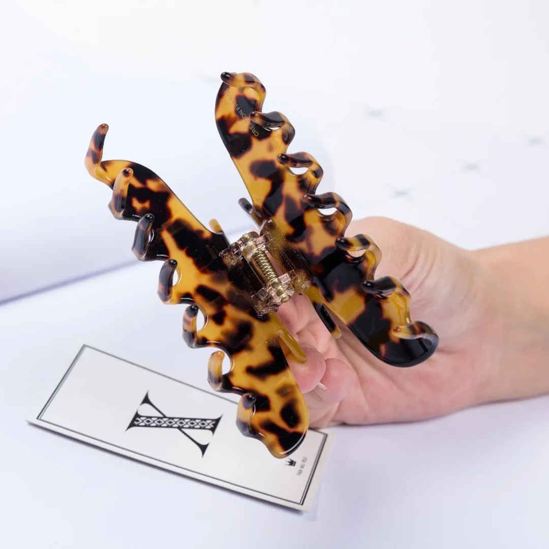 Dark patterned hair clip held by a hand on a white background